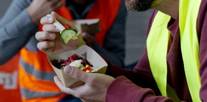 hydrobar-bearded-smiling-worker-wearing-hard-hat-vest-holding-lunch-box-eating-food-break_695242-9715